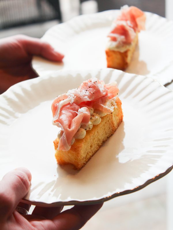 Een bordje met brioche en prosciutto wordt aangereikt